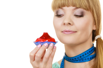Woman undecided with blue measuring tape around her neck holds in hand cake cupcake, trying to resist temptation. Weight loss diet dilemma gluttony concept.